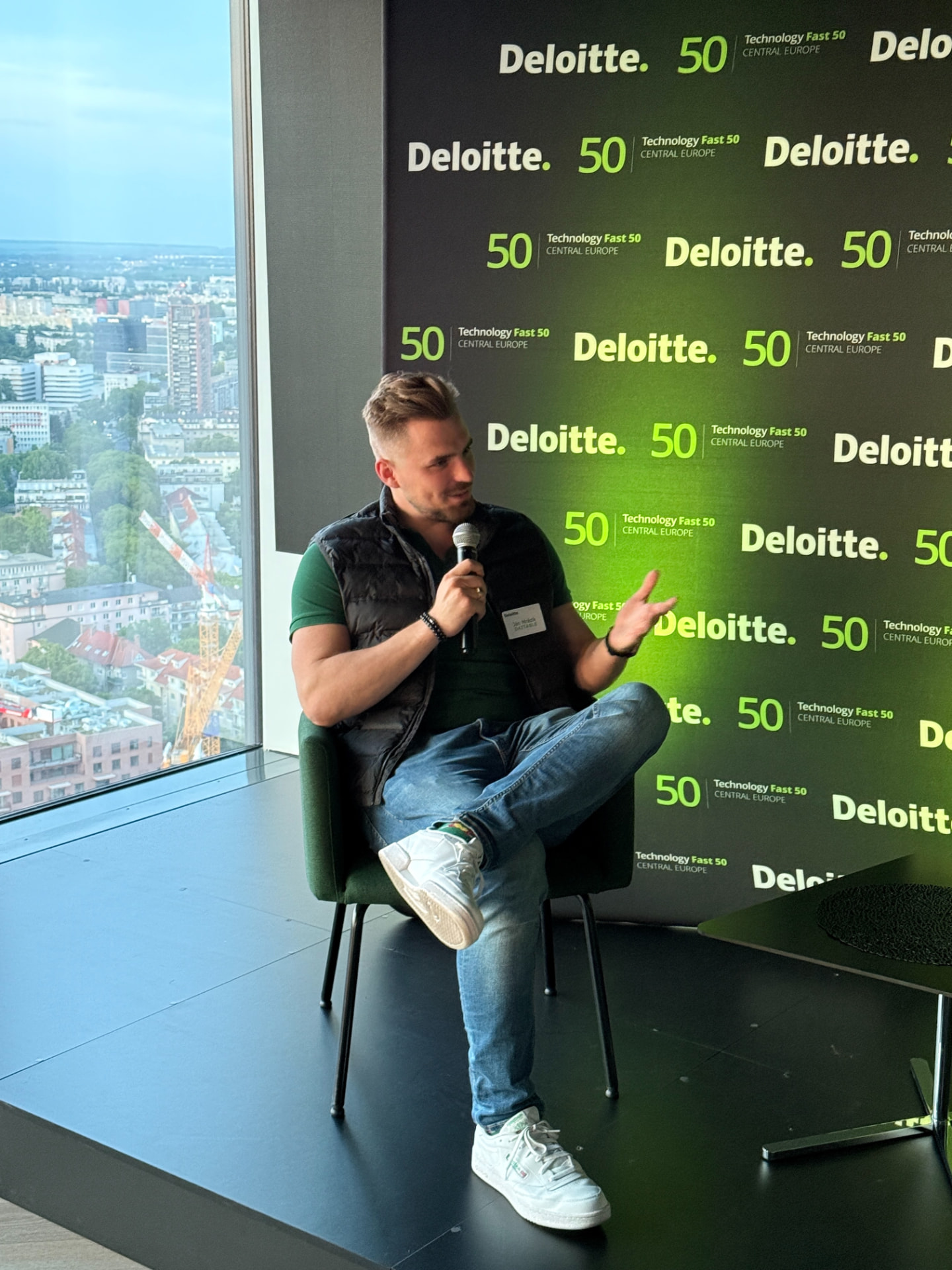 Ján Mrázik vedie diskusiu na podujatí Deloitte Technology Fast 50, sedí v zelenej stoličke s mikrofónom v ruke