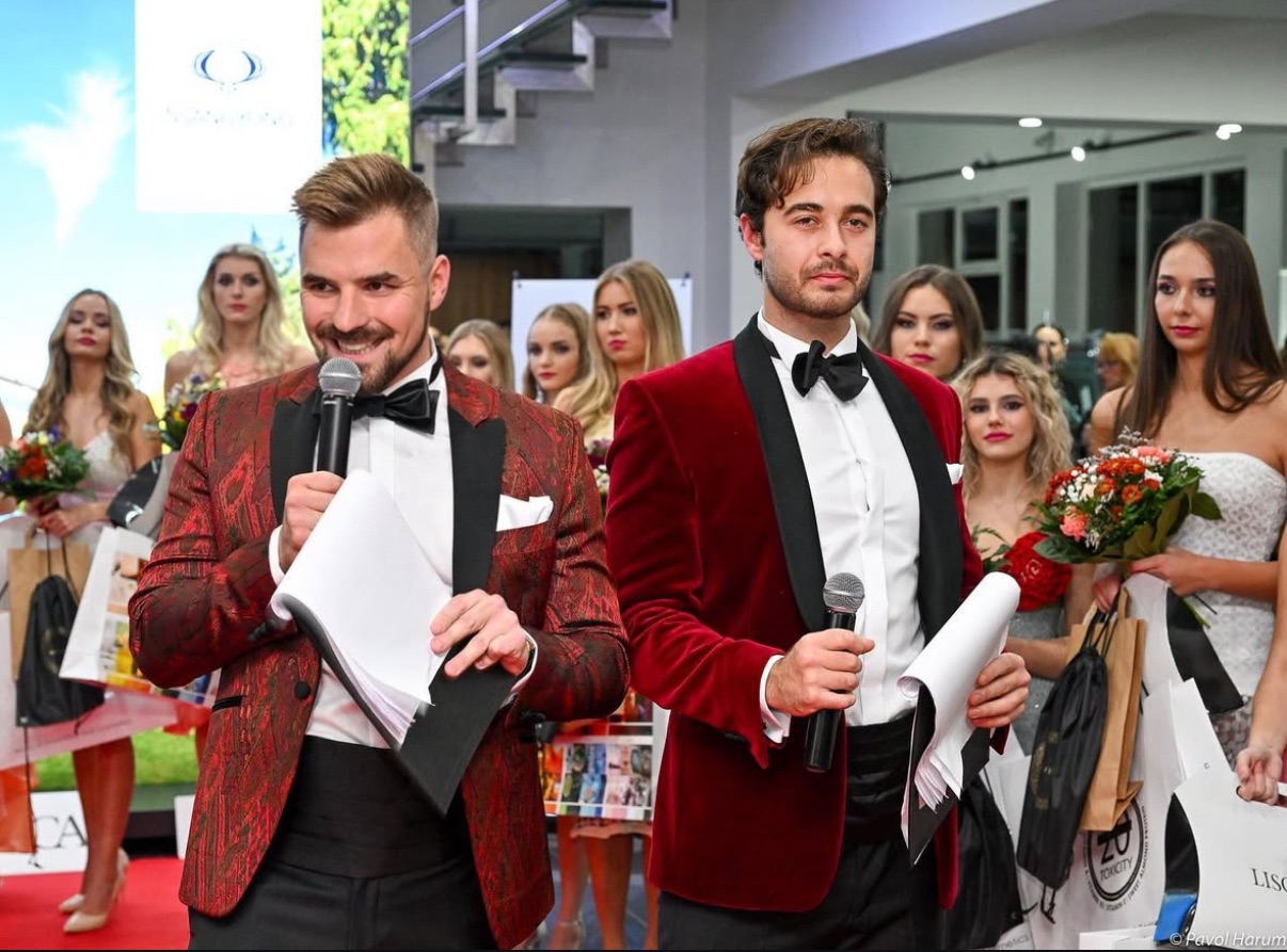 Ján Mrázik moderuje súťaž krásy v červenom saku s mikrofónom v ruke