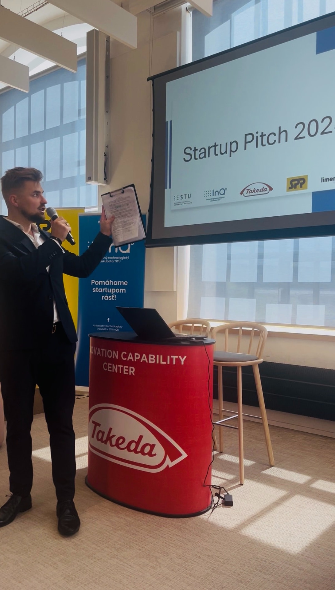 Ján Mrázik moderuje startupový event, drží mikrofón a poznámky pri prezentácii Startup Pitch