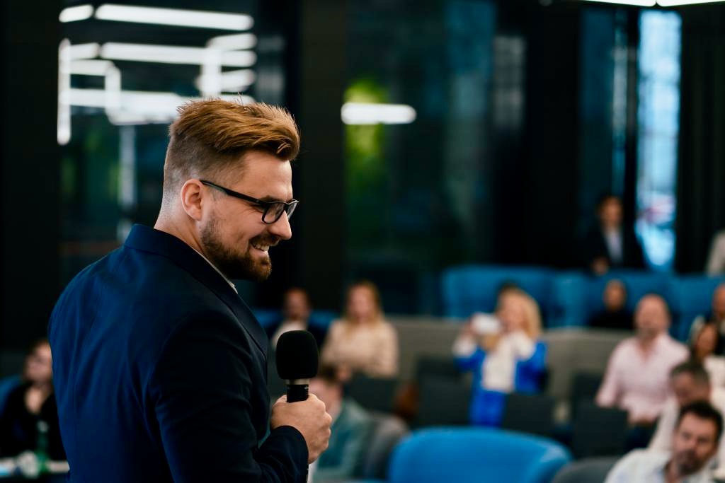 Ján Mrázik vedie firemný event v sále s publikom a mikrofónom v ruke